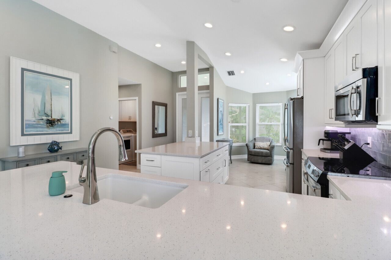 A modern kitchen with a large island, white cabinetry, and stainless steel appliances.