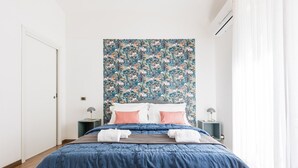 A bedroom with a large bed, floral wallpaper, two bedside tables with lamps, and a white door. - Santamaura Vatican Apartment - 50 meters from the Vatican walls! (Roma)