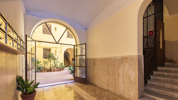 A corridor with a tiled floor, a potted plant, and a staircase with a metal railing. - Santamaura Vatican Apartment - 50 meters from the Vatican walls! (Roma)