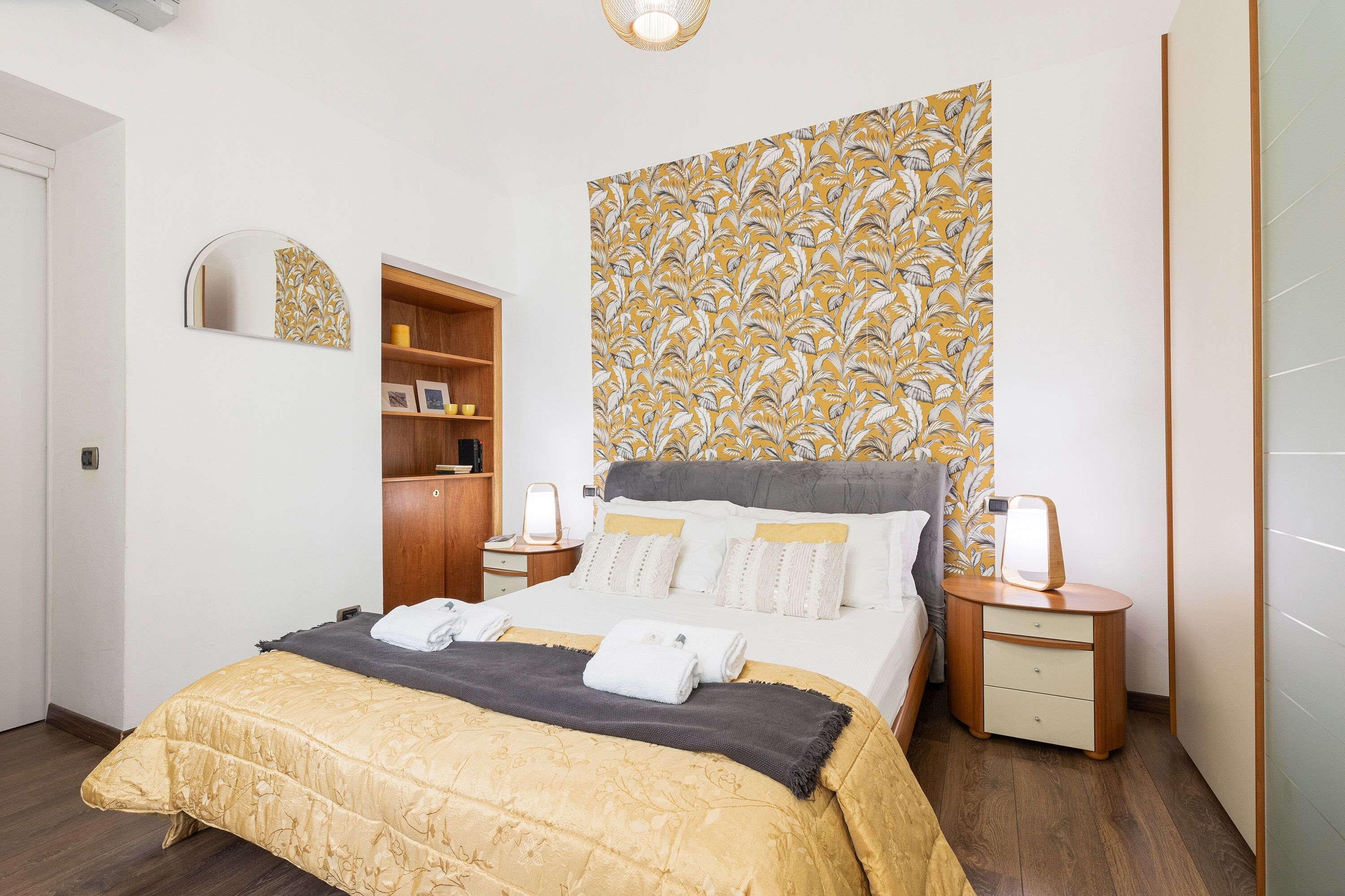 Ein Hotelzimmer mit Bett, Nachttischen, einem Kleiderschrank und einer Wand mit Blättermotiv.