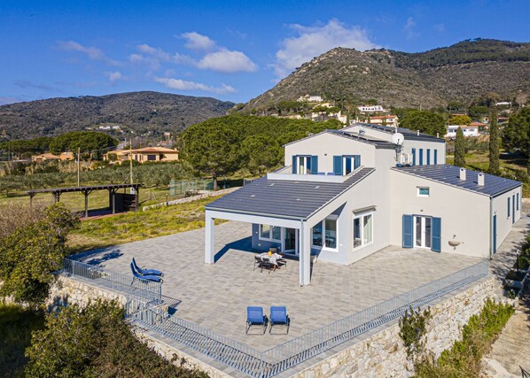 A modern two-story house with a covered patio area, a swimming pool, and a view of the surrounding hills.