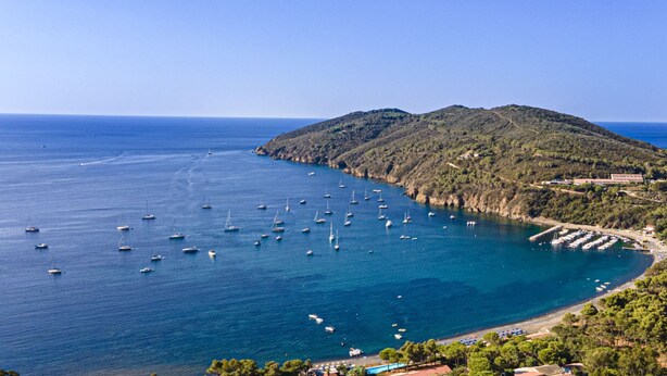 A coastal view with boats, a marina, and a hilly landscape.