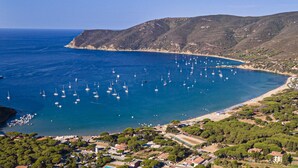 A coastal town with a marina filled with sailboats, surrounded by hills and a clear blue sea.