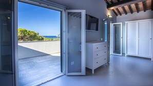 A modern room with a sliding glass door leading to a balcony, a white dresser, a TV mounted on the wall, and a ceiling with exposed beams.