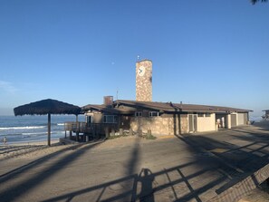 Un bâtiment situé sur la côte, doté d’une tour horlogère, d’un parasol de plage et, au loin, d’une tour de surveillance des sauveteurs.
