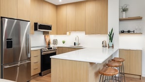 A modern kitchen with wooden cabinets, stainless steel appliances, a large island with bar stools, and a built-in microwave. - Modern Mountain Retreat | Ski-In | Hot Tub (Whistler)