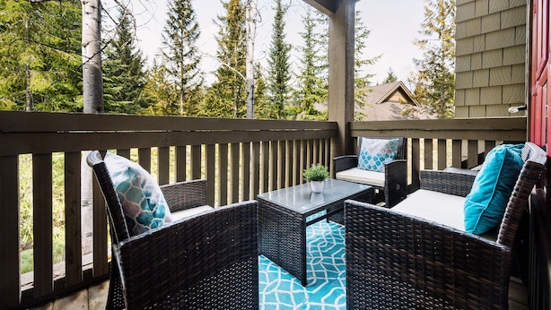 A covered outdoor seating area with wicker furniture and a view of trees. - Modern Mountain Retreat | Ski-In | Hot Tub (Whistler)