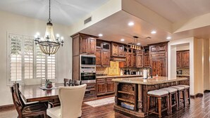 A spacious kitchen with wooden cabinets, a large island with bar stools, and a chandelier. - Private Pool, Pool Table, BBQ, Near San Diego Padres & Seattle Mariners Spring Training + FREE GOLF! (Glendale)
