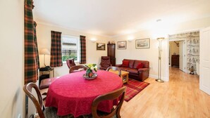 A cozy living room with a red-covered table, a brown leather sofa, and plaid curtains. - Earnside Cottage, Tranquil Escape in Comrie (Comrie)