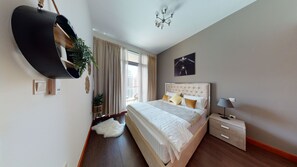 A modern bedroom with a large bed, a bedside table, a hanging plant, and a view of the city through the window.