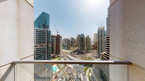 A high-rise building with a glass facade, a construction crane, and a view of a cityscape with multiple buildings and a body of water.