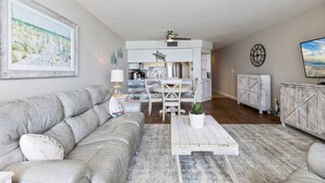 A modern living room with a grey sofa, a coffee table, and a kitchen in the background. - Perfect 1 Bedroom Oceanfront!! (Murrells Inlet)