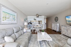 A modern living room with a grey sofa, a coffee table, and a kitchen in the background.