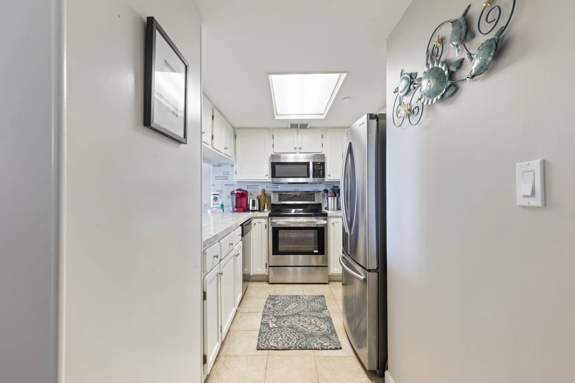 A modern kitchen with white cabinets, stainless steel appliances, a skylight, and a decorative wall piece.