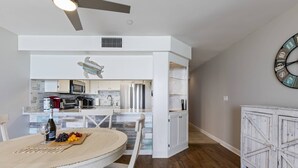 A modern kitchen with white cabinetry, a dining area with a round table, and a clock on the wall. - Perfect 1 Bedroom Oceanfront!! (Murrells Inlet)