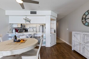 A modern kitchen with white cabinetry, a dining area with a round table, and a clock on the wall.