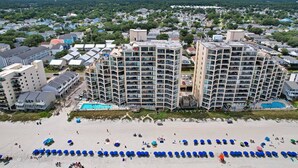 A beachfront hotel with multiple high-rise buildings, a sandy beach with umbrellas, and a clear view of the surrounding residential area. - Perfect 1 Bedroom Oceanfront!! (Murrells Inlet)