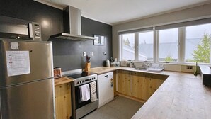 Een moderne keuken met een roestvrijstalen koelkast, oven en vaatwasser, houten kastjes en een groot raam met uitzicht.