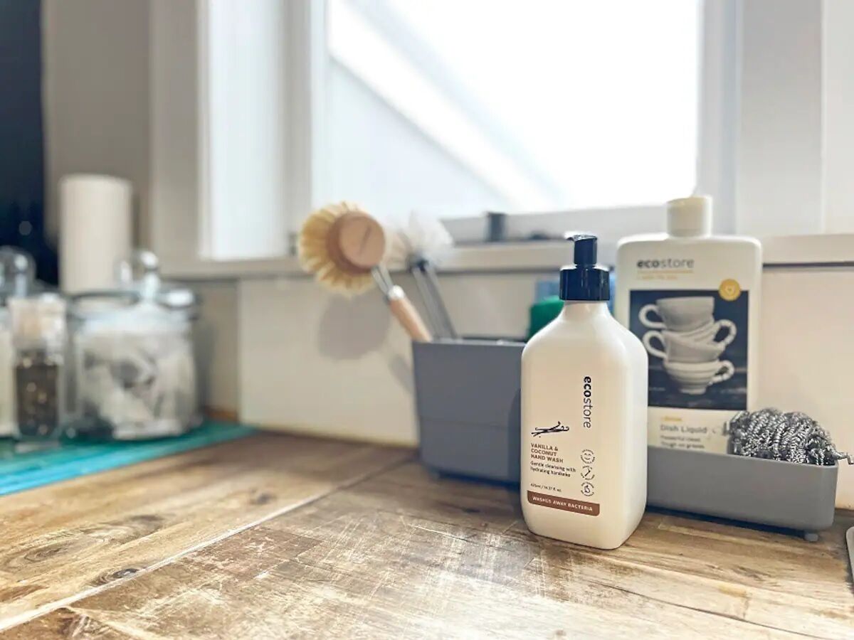 A bathroom vanity with a white bottle of hand wash, a blue bottle, and a box of dish liquid.