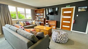 Een woonkamer met een grijze bank, een houten salontafel, een ottoman met dessin, een boekenkast en een televisie.