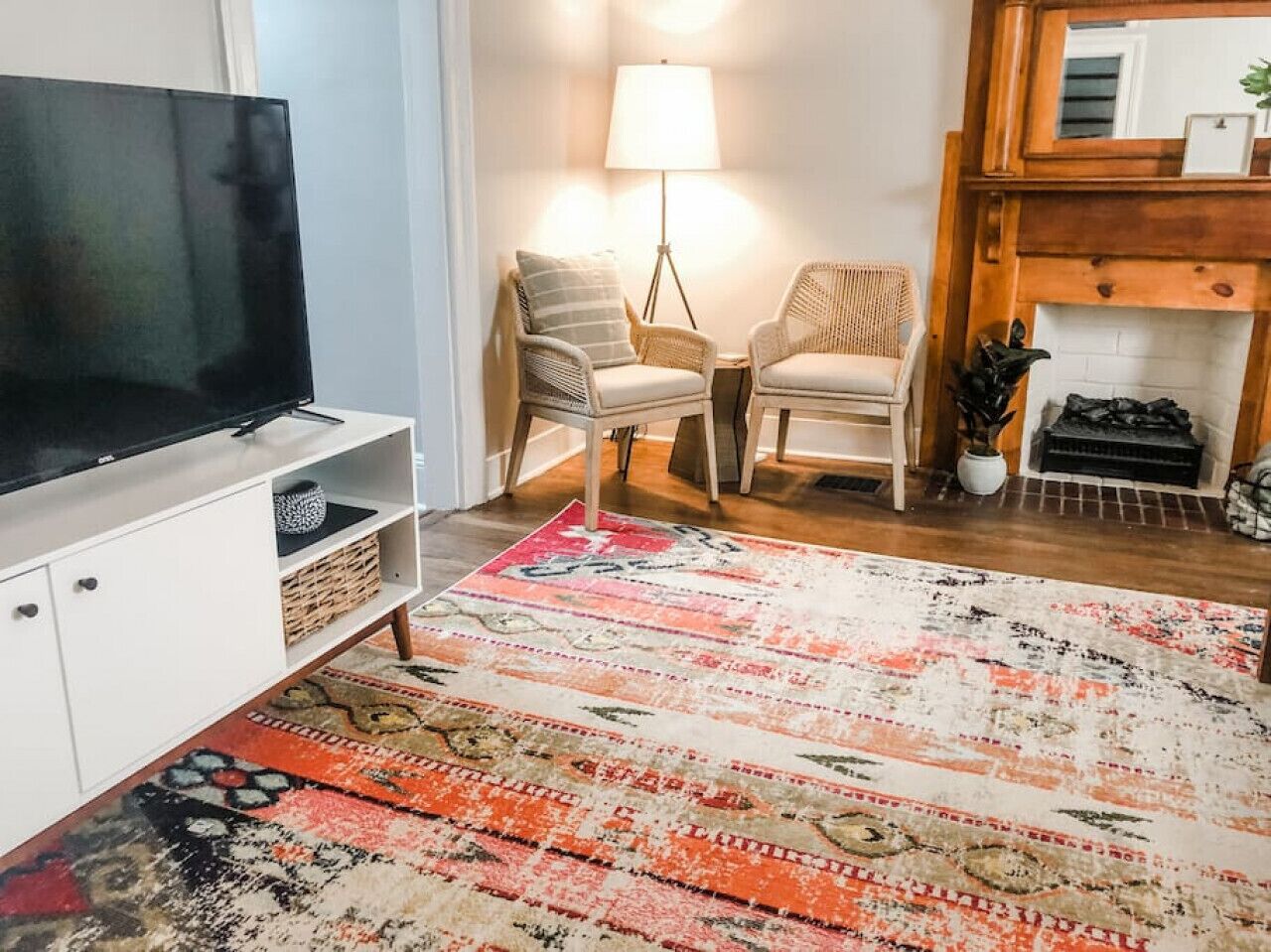 A living room with a flat-screen TV, two wicker chairs, a patterned rug, and a fireplace.