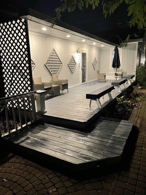 A covered outdoor seating area with a wooden deck, wicker furniture, and a black umbrella.
