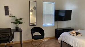 Une chambre à coucher comprenant un lit, un bureau, une chaise, un téléviseur, une fenêtre avec des stores et un miroir.