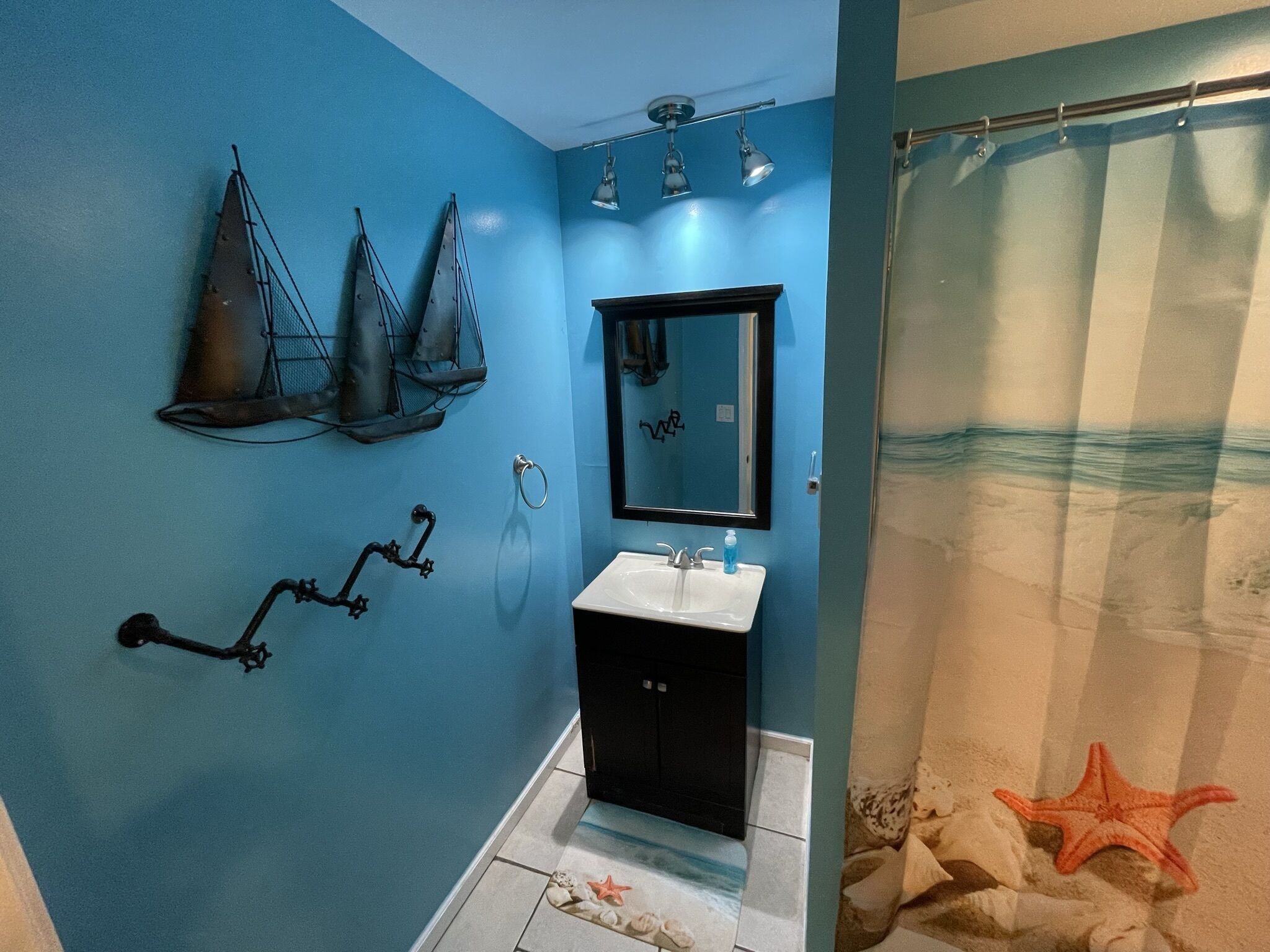 A bathroom with a blue wall, a black sink, and a shower curtain with a beach scene.