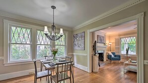 A dining area with a wooden table and chairs, a chandelier, and large windows with a view of greenery. - Bright Greensboro Escape ~ 1 Mi to Downtown (Greensboro)