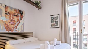 A hotel room with a large bed, a wooden headboard, a painting on the wall, a framed picture, and a balcony with a view of buildings. - Duplex en Las Ramblas: tu refugio en BCN (Barcelona)