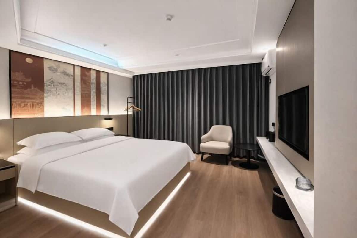 A modern hotel room with a large bed, a seating area, a flat-screen TV, and artwork on the wall.