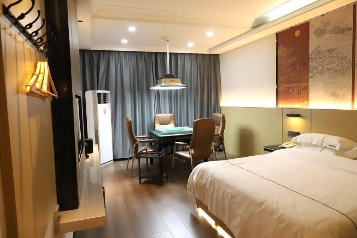 A hotel room with a bed, desk, chairs, and an air conditioning unit.