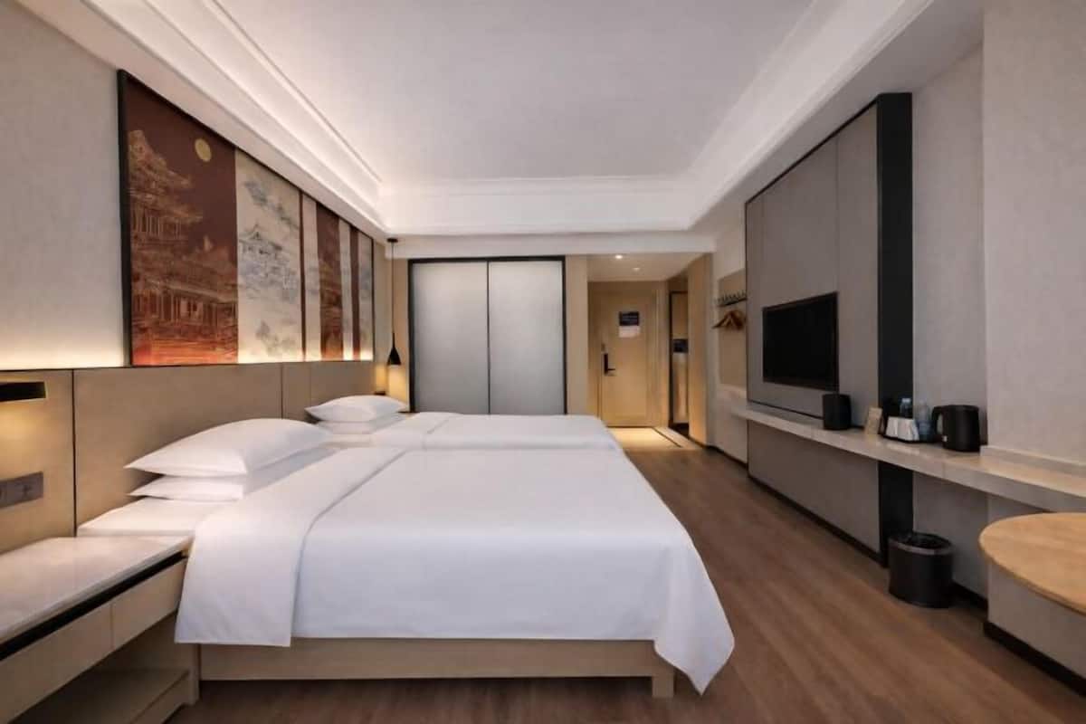 A modern hotel room with a large bed, bedside tables, a TV, and artwork on the wall.