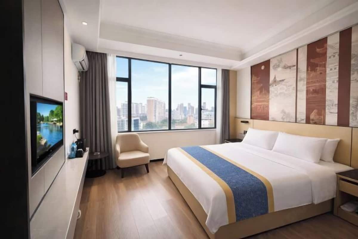 A hotel room with a large bed, a television, a chair, and a city view.