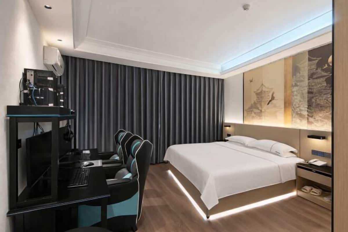 A modern hotel room with a desk, computer, and chair, a large bed, and a wall with artwork.
