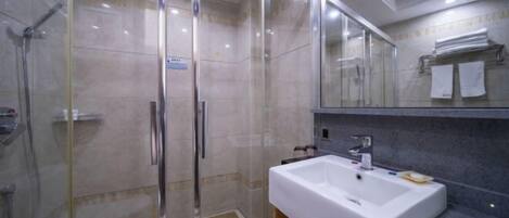 Un baño moderno con ducha envuelta en vidrio, un lavamanos blanco y un espejo sobre él.