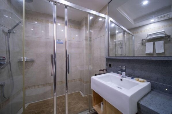 A modern bathroom with a glass-enclosed shower, a white sink, and a mirror above the sink. - Huangsheng Hotel (Shanggao)