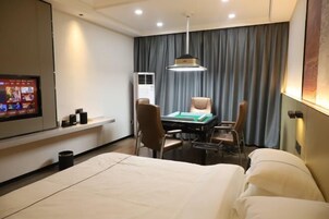 Habitación de hotel con una cama, un escritorio con sillas, un televisor y un ventanal con cortinas.