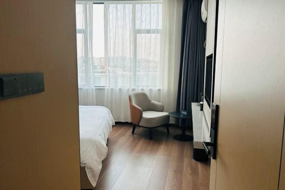 A hotel room with a bed, a chair, a small table, and a TV.