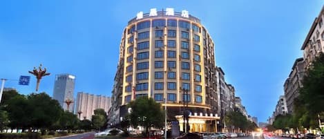 Un hotel de varios pisos con fachada curva, situado en una calle de la ciudad con paso de peatones.