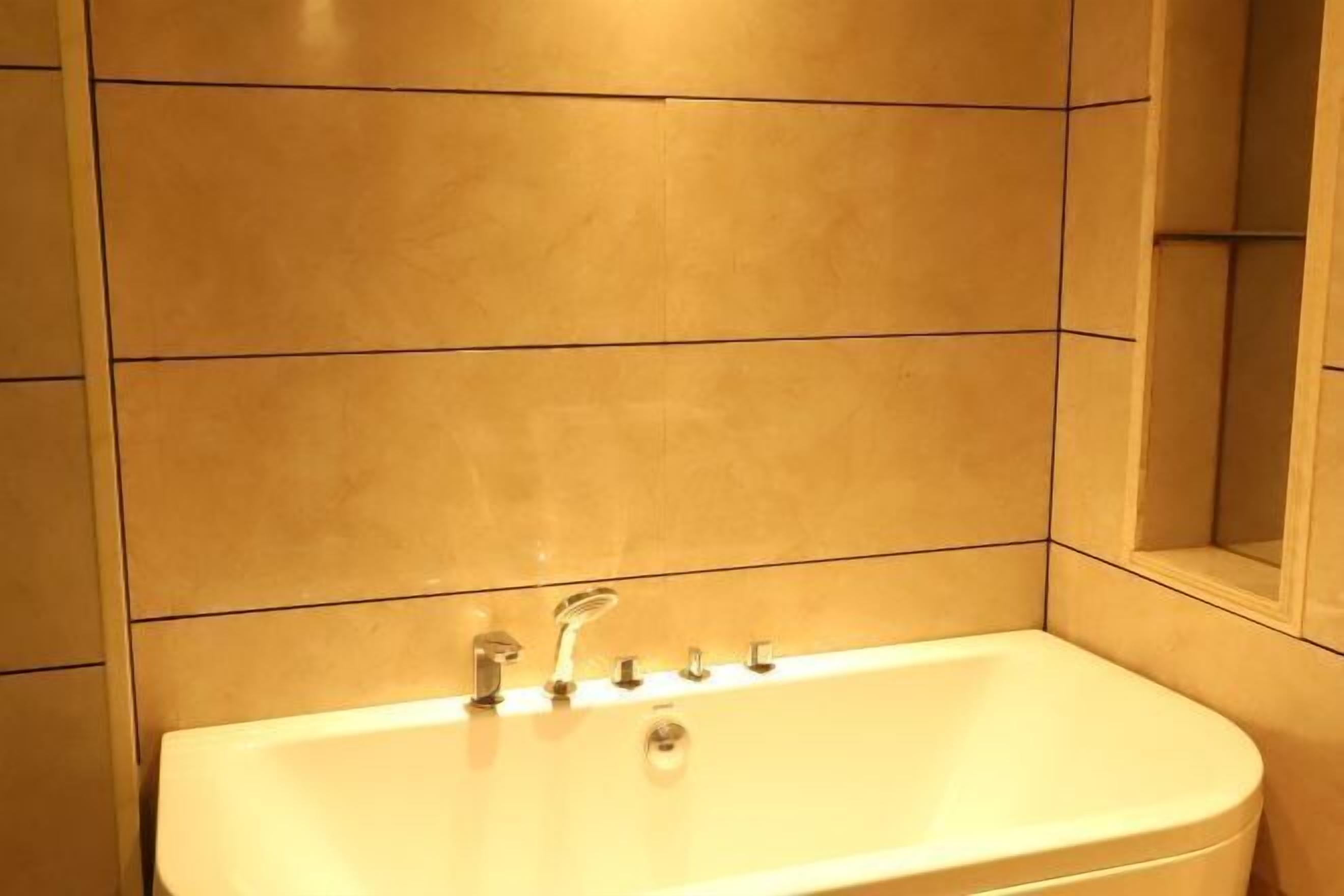Un baño con bañera, espejo y paredes de azulejos.