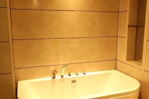 A bathroom with a bathtub, a mirror, and tiled walls. - Huangsheng Hotel (Shanggao)