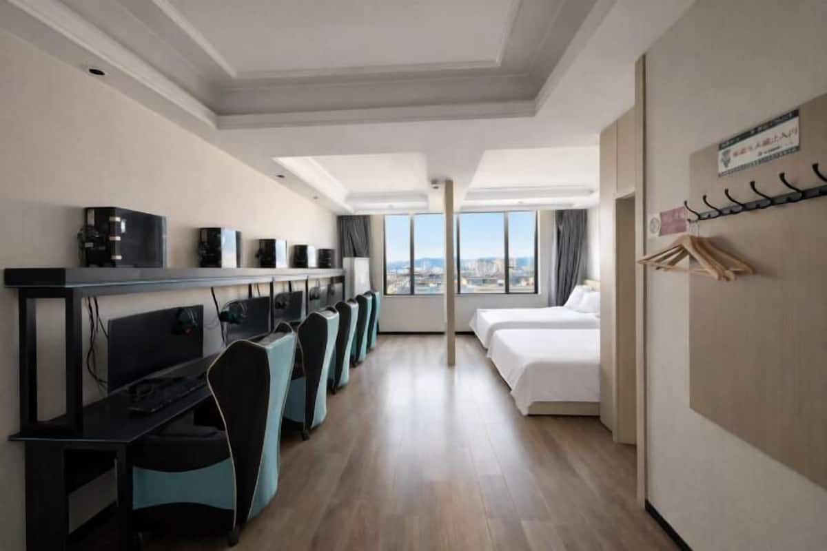 A hotel room with a desk, chairs, a bed, and a view of the city.