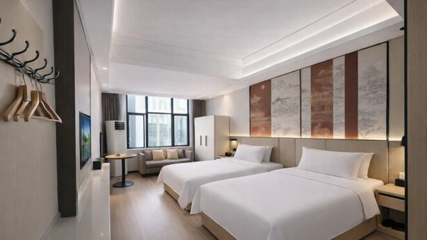 Une chambre d’hôtel moderne avec deux lits, un canapé, une petite table et des œuvres d’art accrochées aux murs.