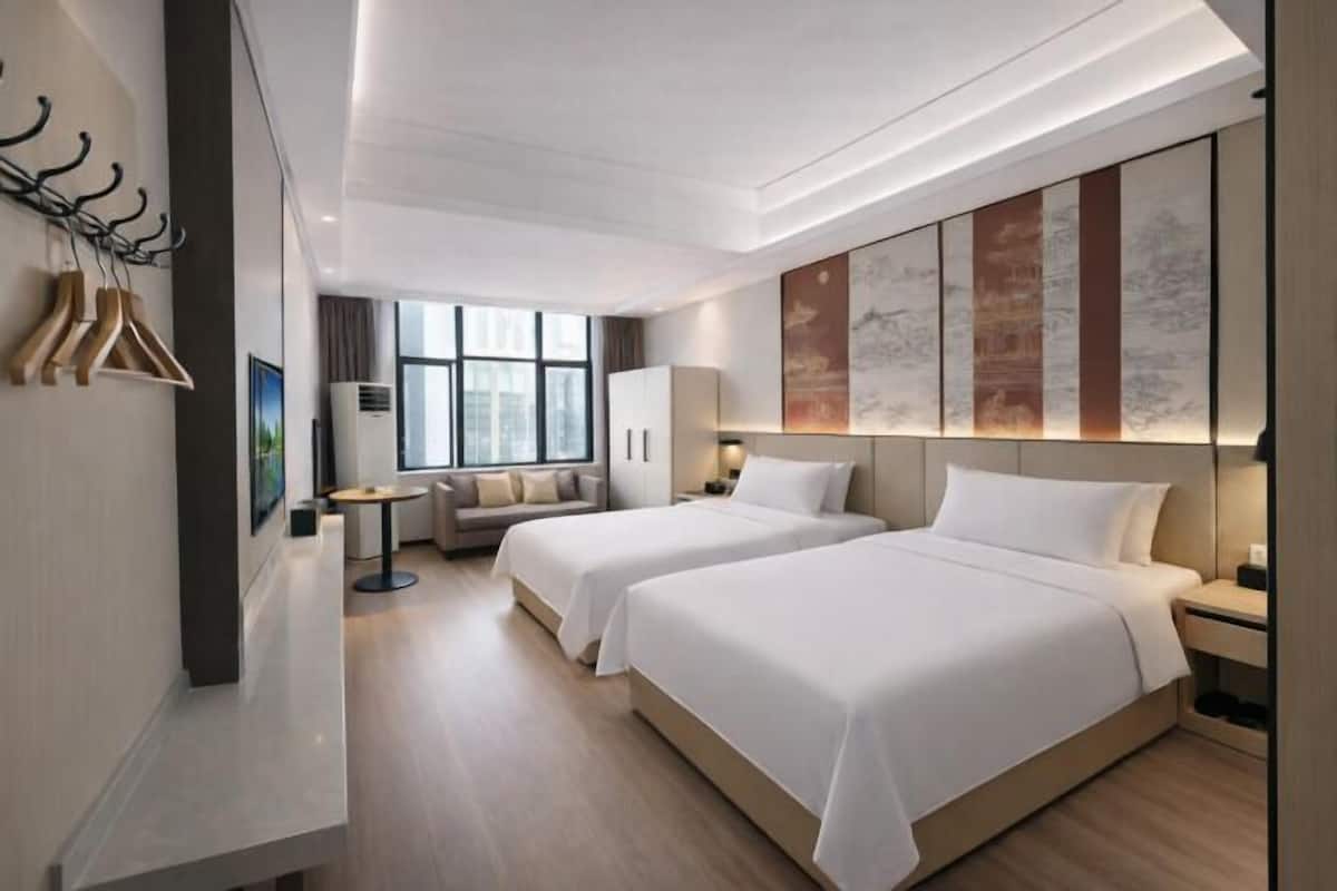 A modern hotel room with two beds, a sofa, a small table, and artwork on the walls.