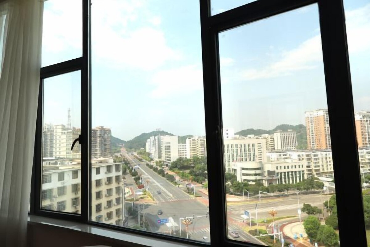 A view from a window with multiple panes, overlooking a cityscape with buildings, roads, and greenery.