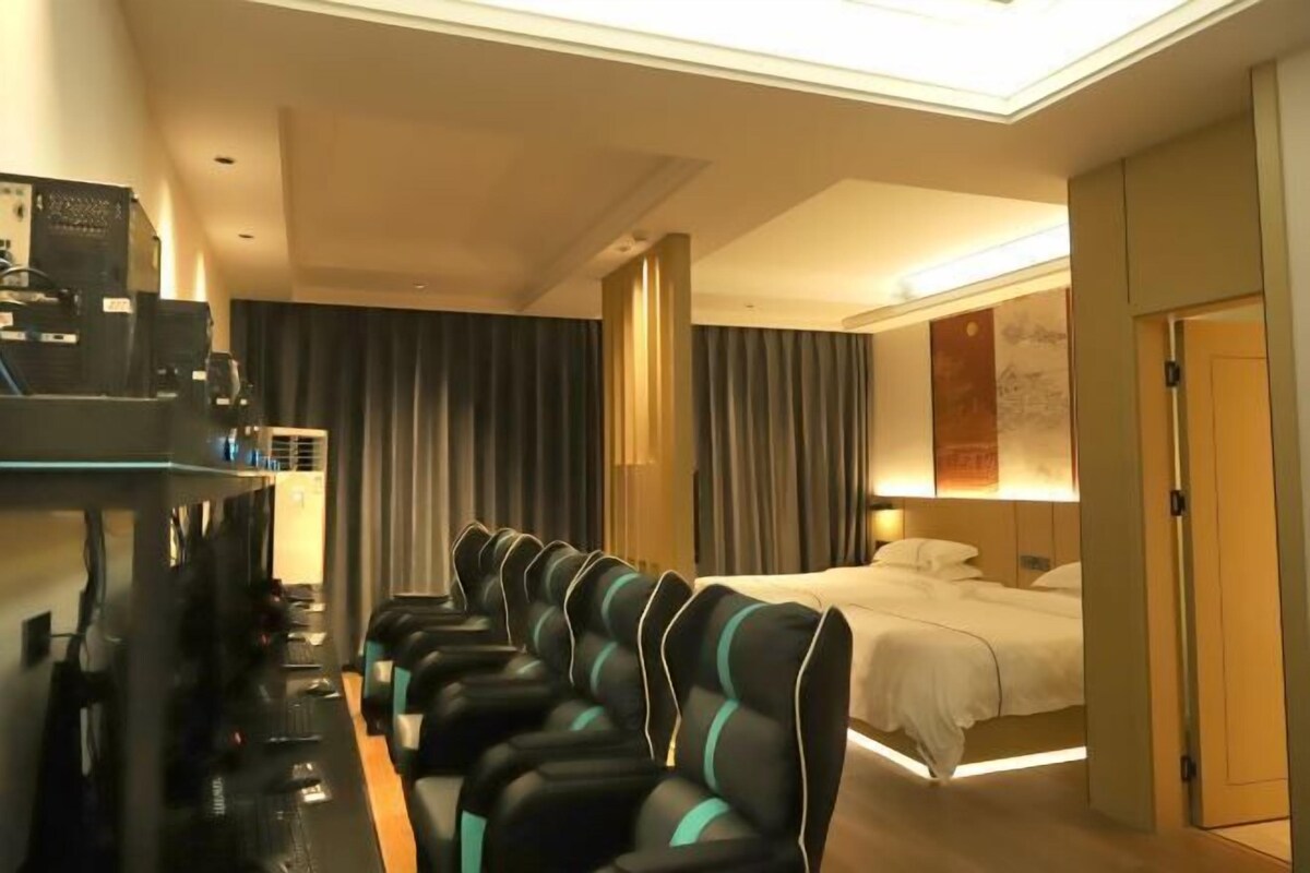 A hotel room with a bed, a desk with a computer, and a massage chair.