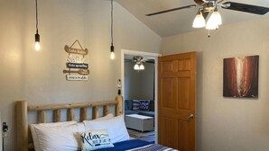 Quarto com cama, ventilador de teto, luminária na parede e porta.