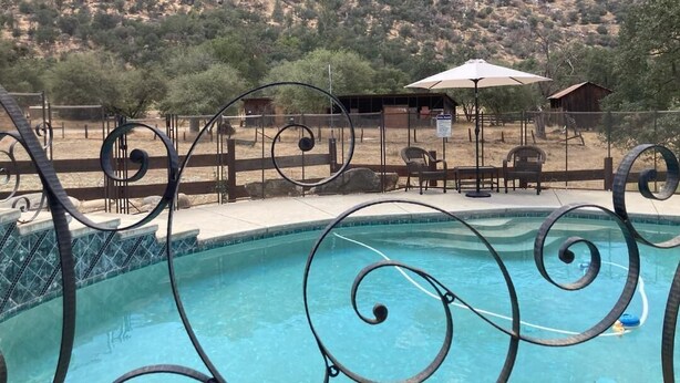 Uma piscina com grade de metal e design em espiral, rodeada por móveis de exterior e um cenário montanhoso.