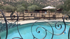 Une piscine entourée d’une clôture en métal au design en spirale, agrémentée de mobilier d’extérieur et offrant une vue sur les montagnes.